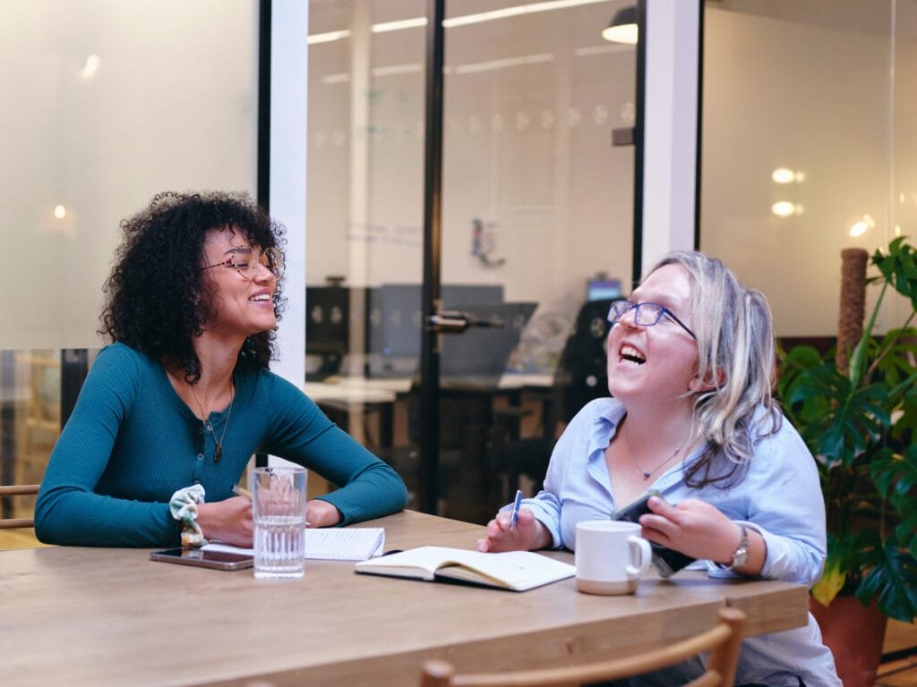 UK, London, Two smiling women writing in notebooks in modern off
